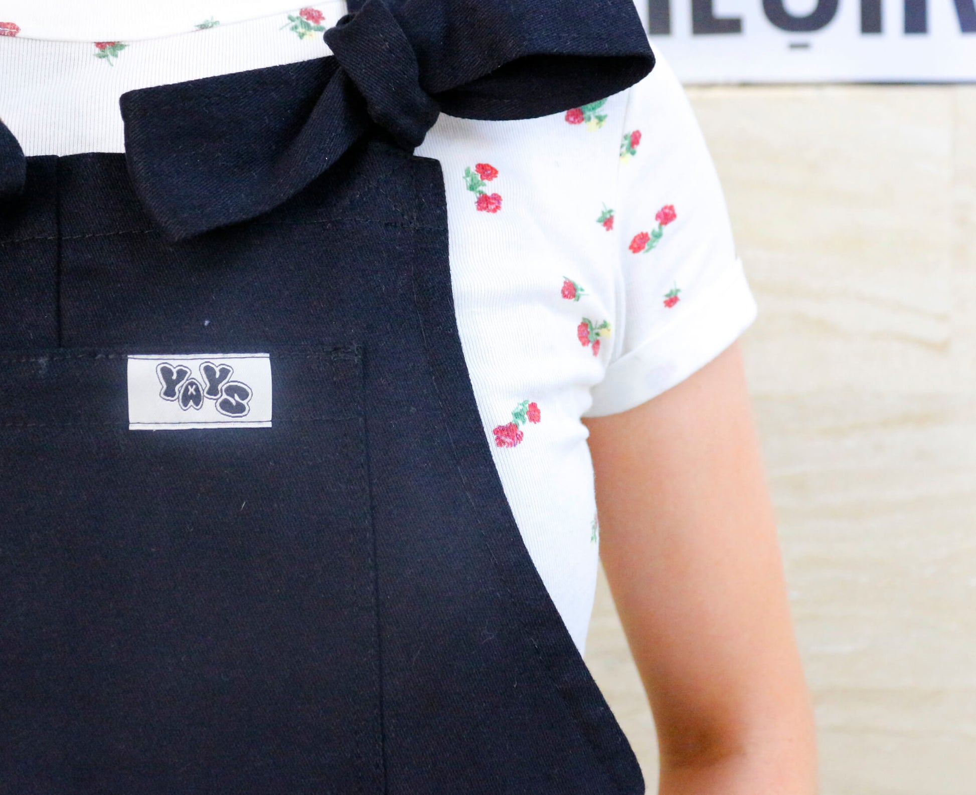 woman wearing YAYS unisex cotton dungaree in Raven Black, front view close-up on front pocket and YAYS logo